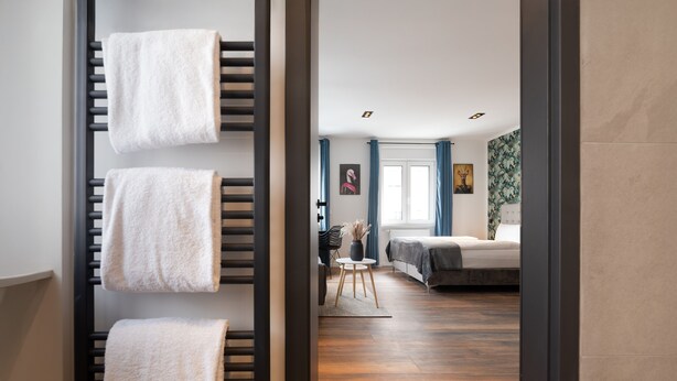 Un dormitorio moderno con suelo de madera, una cama, una mesita y una silla.