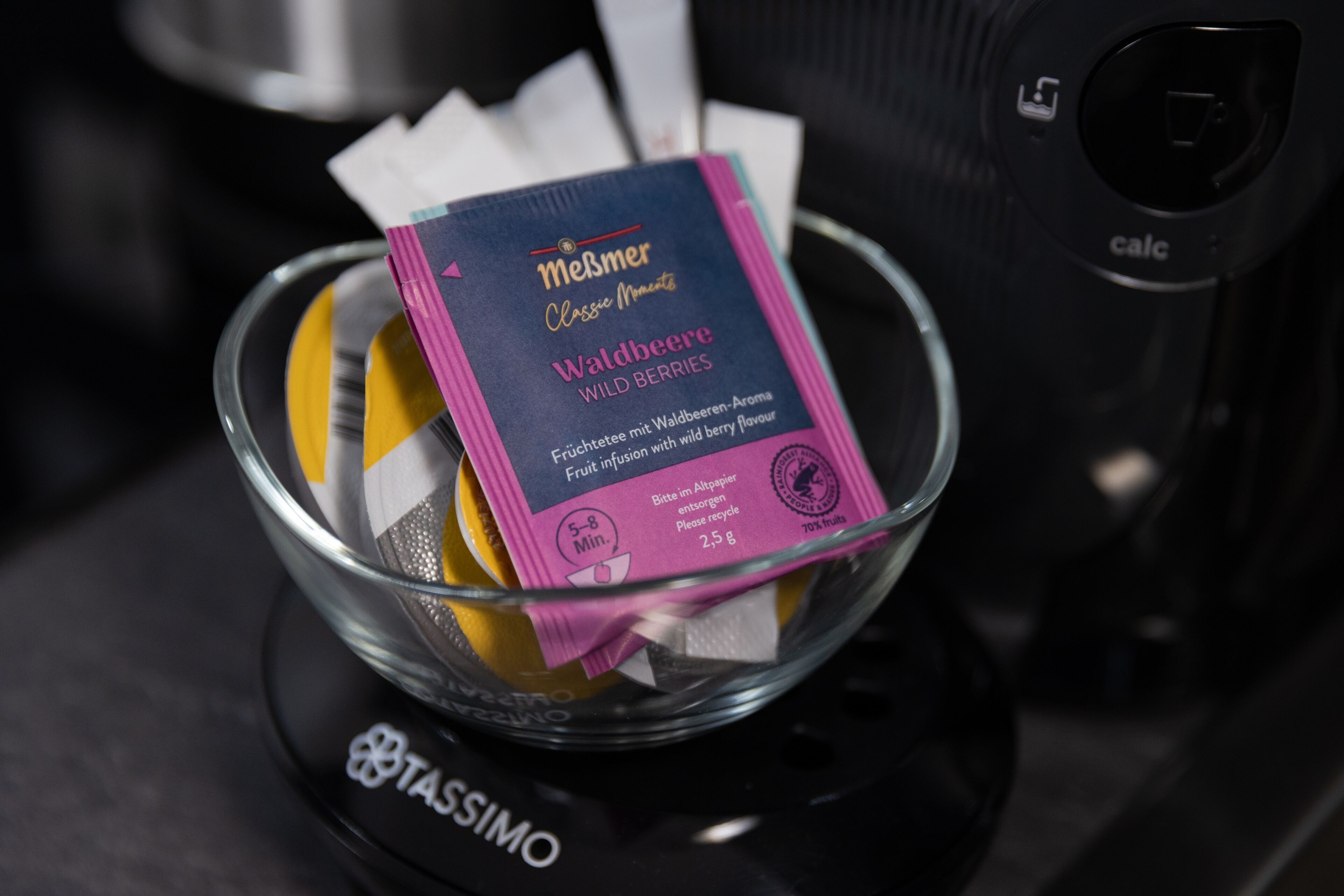 A glass bowl containing a packet of Meßmer Classic Moments Wild Berries on a TASSIMO coffee machine.