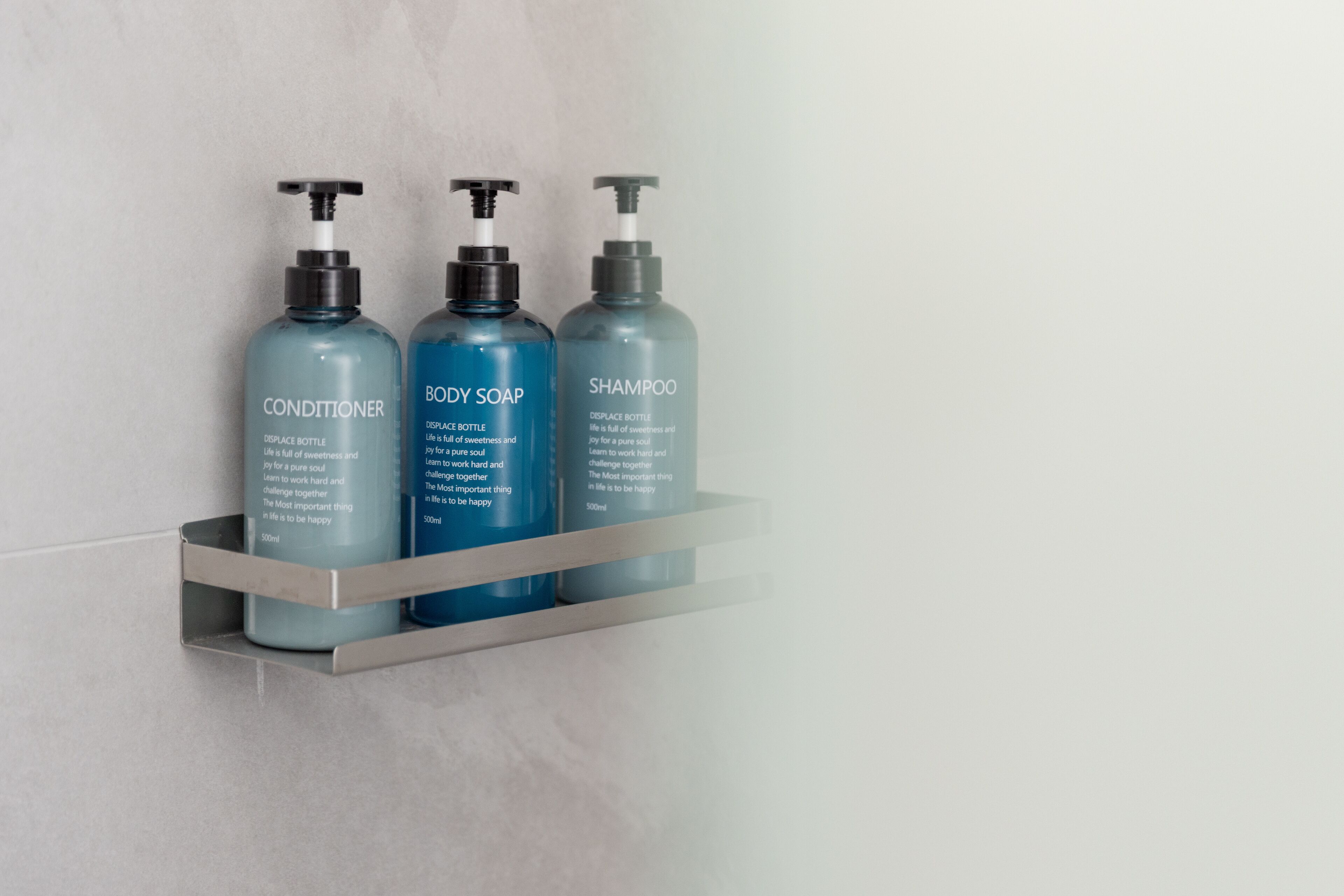 Three bottles of personal care products on a metal shelf against a wall.