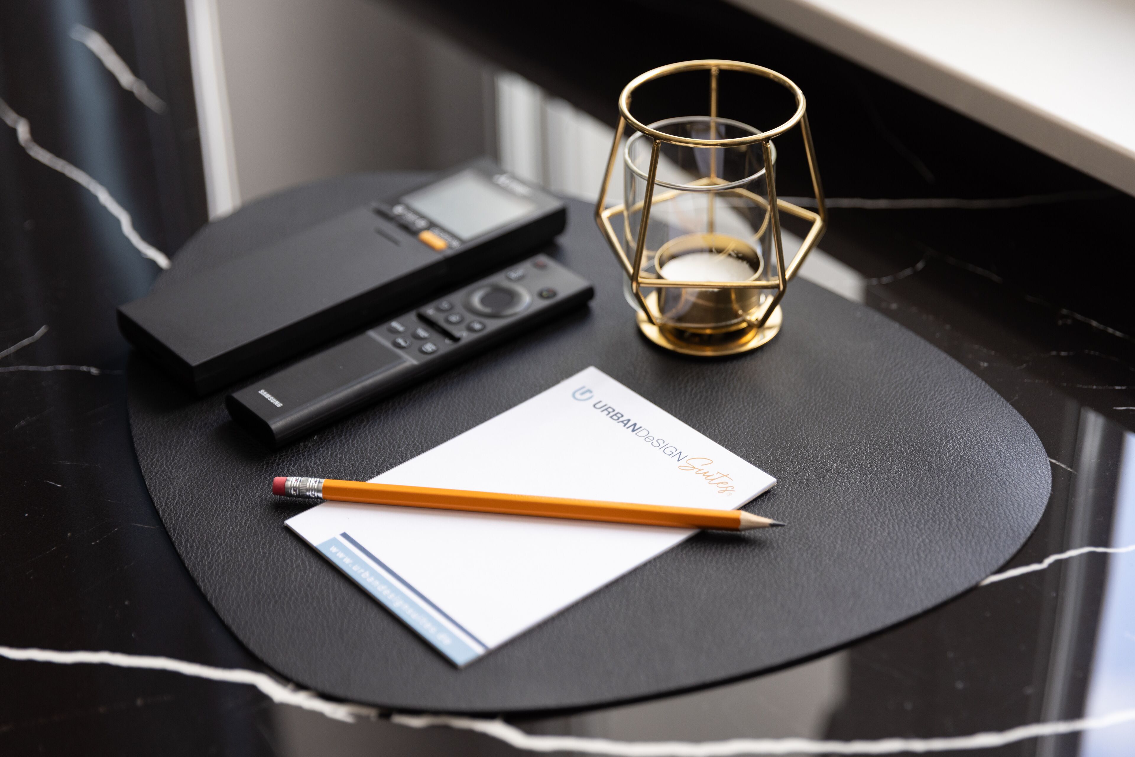 Una mesa de mármol negro con un cuaderno, un lápiz y un pequeño dispositivo electrónico negro.