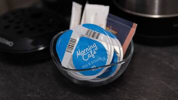 En glasskål som innehåller ett blått paket märkt med texten ”Morning Café” och en streckkod, placerad på en mörk yta.