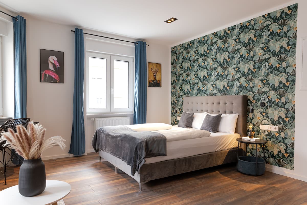A bedroom with a bed, a round table with a vase, and a wall with a floral pattern.