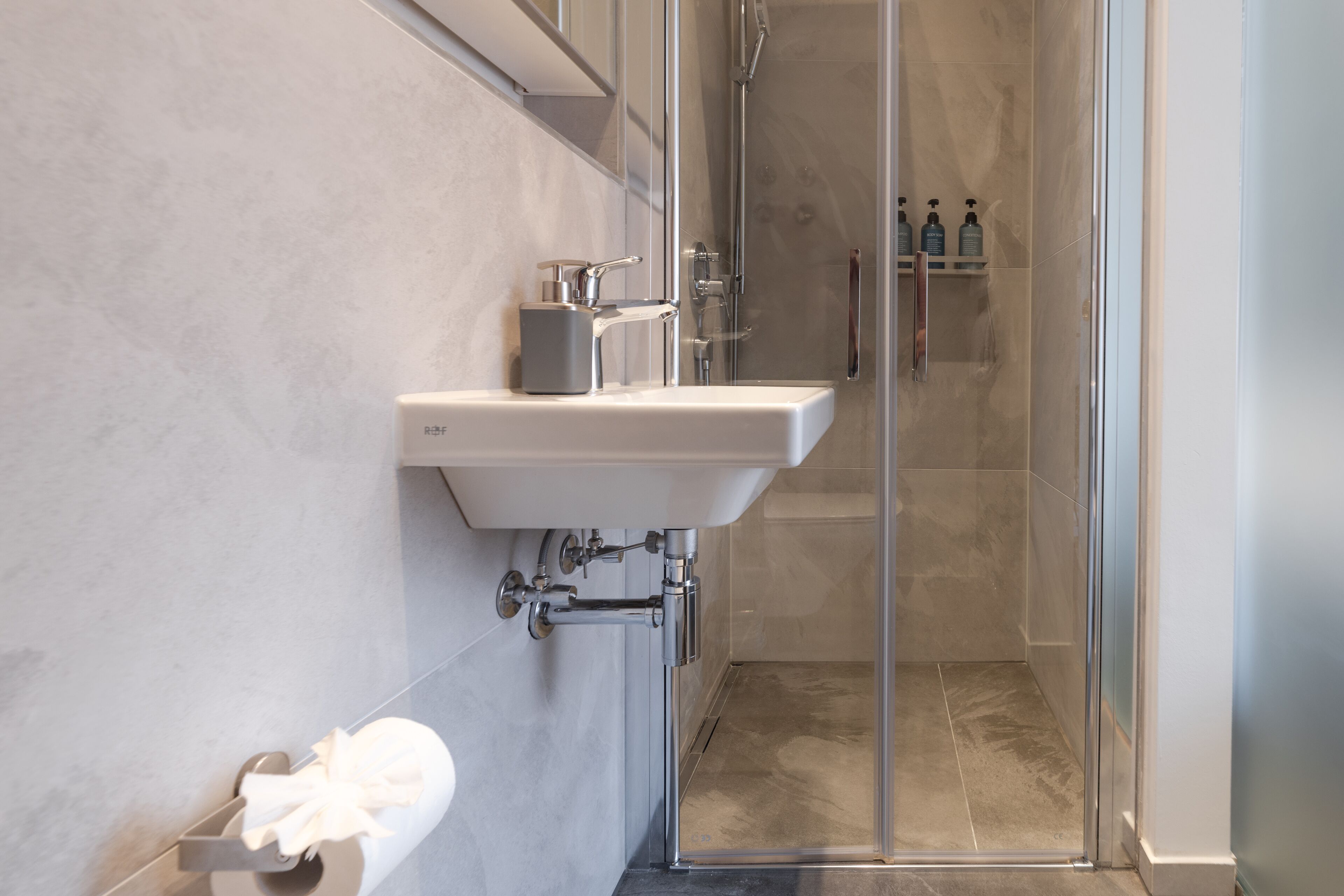 A modern bathroom with a glass shower enclosure, a white sink, and a towel rack.