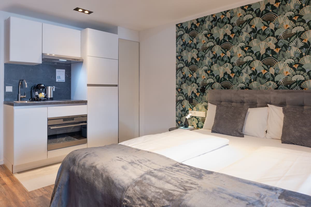 A modern hotel room with a bed, a small kitchenette, and a patterned wallpaper.