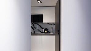 Una cocina moderna con armarios blancos, salpicadero de mármol y cafetera de acero inoxidable.