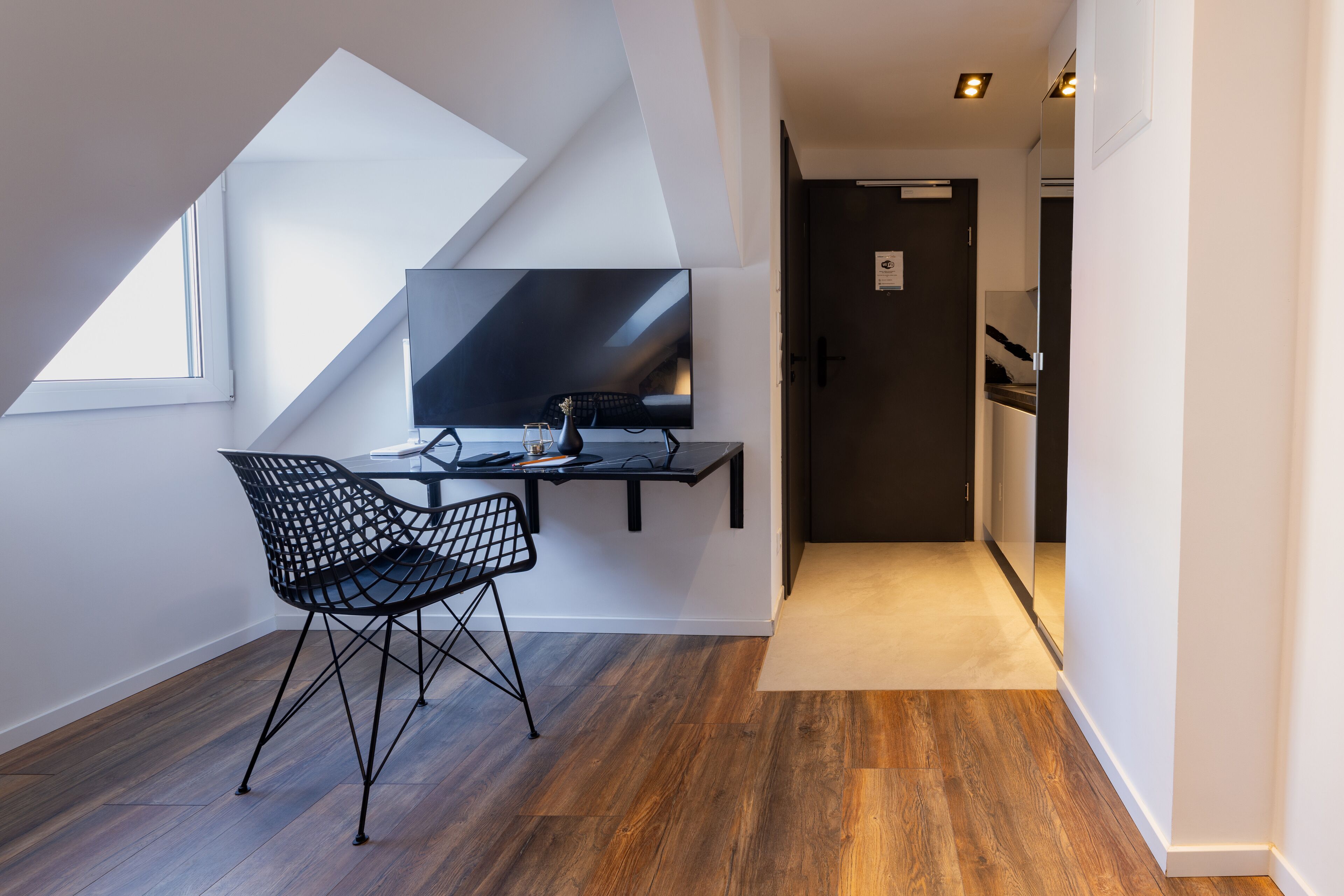 Ein modernes Zimmer mit Schreibtisch, Stuhl und einem großen Flachbildfernseher.