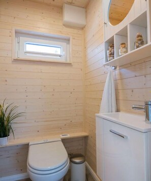 Ein Badezimmer mit Holzverkleidung, einer Toilette, einem Waschbecken und einem kleinen Fenster über der Toilette.