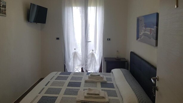 Une chambre à coucher avec un lit, une télévision, un tableau et une fenêtre avec des rideaux.