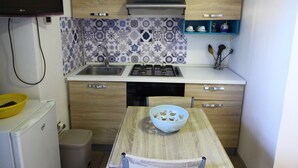 Une cuisine compacte dotée d’une cuisinière intégrée, d’un évier et de meubles de rangement en bois. On peut également apercevoir un petit réfrigérateur et une poubelle.