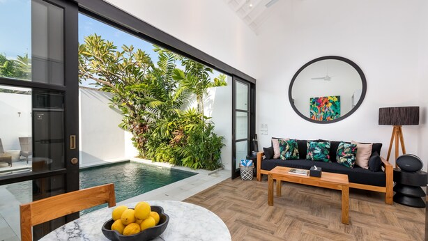 A modern living room with a pool, a black sofa with colorful cushions, and a round mirror on the wall. - Villa Jabula  (Seminyak)