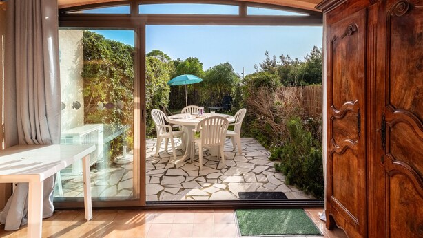 Um pátio com mesa e cadeiras, um armário de madeira e uma porta de vidro que dá para o exterior.