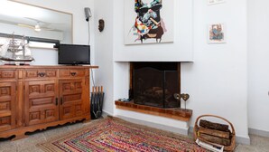 A living room with a wooden cabinet, a flat-screen TV, a colorful rug, a fireplace, and wall art. - Atic Cap Tossa by Interhome (Tossa de Mar)