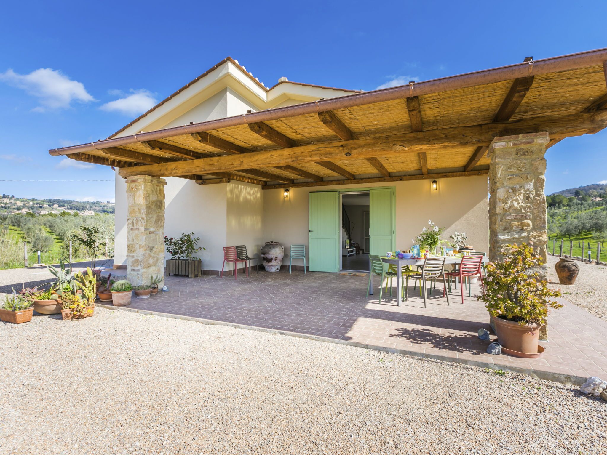 Un patio cubierto con mobiliario exterior, pilares de piedra y plantas en macetas.