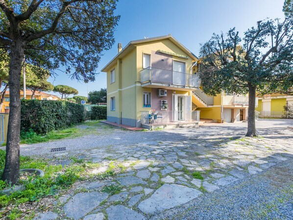 A yellow two-story building with a balcony, surrounded by trees and a cobblestone courtyard. - Casa e mare by Interhome (Cecina)