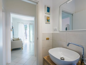 A modern bathroom with a white sink, a large mirror, and a door leading to a living area with a sofa and a view of the outdoors. - Casa e mare by Interhome (Cecina)