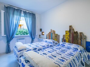 A bedroom with two beds, a window with blue curtains, and a wall with wooden panels. - Casa e mare by Interhome (Cecina)