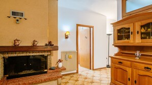 A cozy living room with a fireplace, wooden cabinets, and a tiled floor. - Apartment Fruet by Interhome (Lago di Caldonazzo)