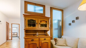 A room with a wooden cabinet with glass doors, a beige sofa, and a tiled floor. - Apartment Fruet by Interhome (Lago di Caldonazzo)