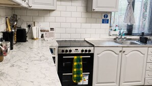 Una cocina con armarios blancos, una estufa negra, una ventana con persianas y una toalla de cuadros colgada en el horno.