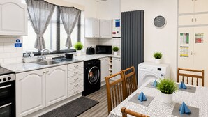 A compact kitchen with a washing machine, microwave, and a dining area with a table and chairs. - Newtons Lodge: Cosy 3-Bed Home, Cul-de-Sac, Free Parking, NTU & QMC Nearby (Nottingham)