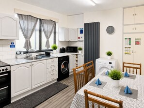 Ett kompakt kök med tvättmaskin, mikrovågsugn och en matplats med bord och stolar.