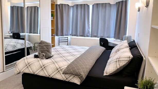 A modern bedroom with a large bed, a mirror, a desk, and a radiator. - Newtons Lodge: Cosy 3-Bed Home, Cul-de-Sac, Free Parking, NTU & QMC Nearby (Nottingham)