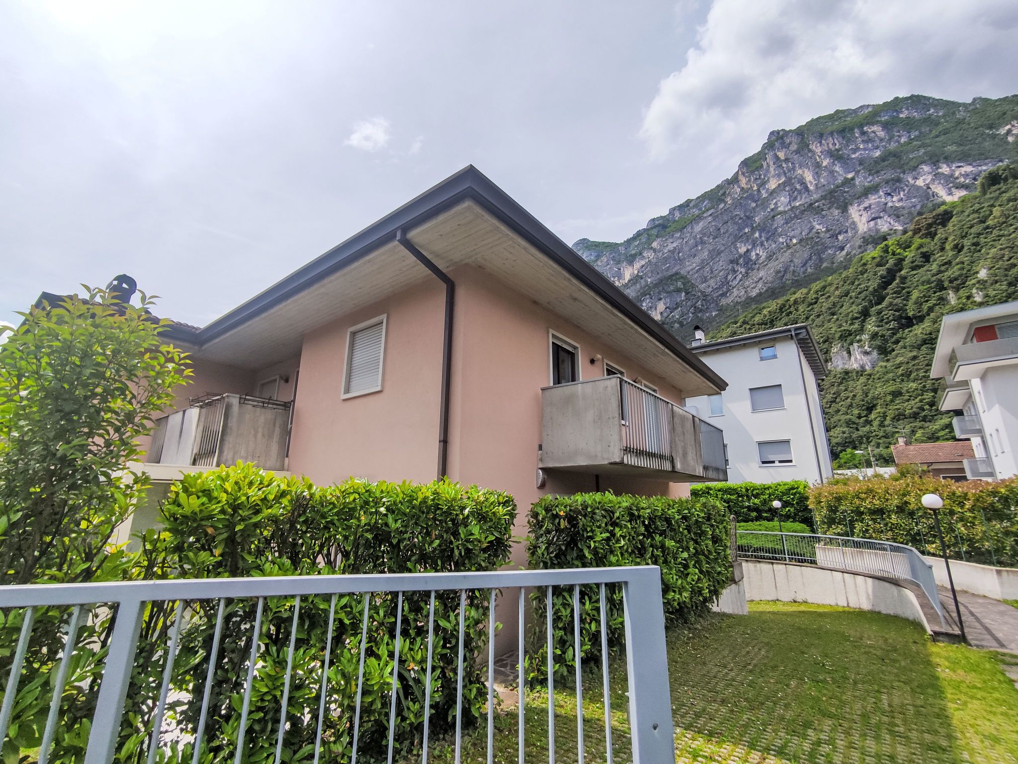 Un bâtiment à deux étages doté d’un balcon, entouré de verdure et avec des montagnes en arrière-plan.