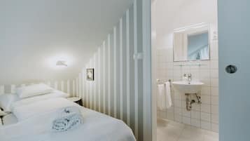 Hotelkamer met een bed, nachtkastje, spiegel aan de muur en een badkamer met wastafel en handdoekhouder.