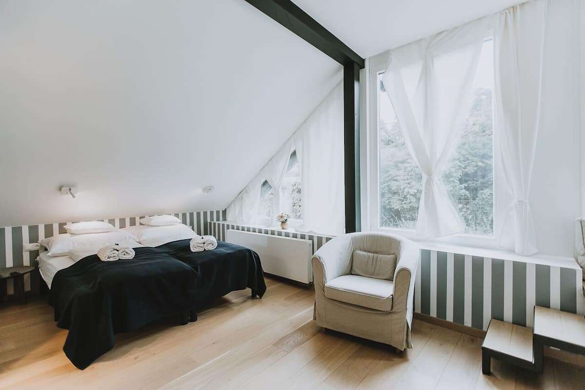 Un dormitorio con cama, una silla y una ventana con cortinas.