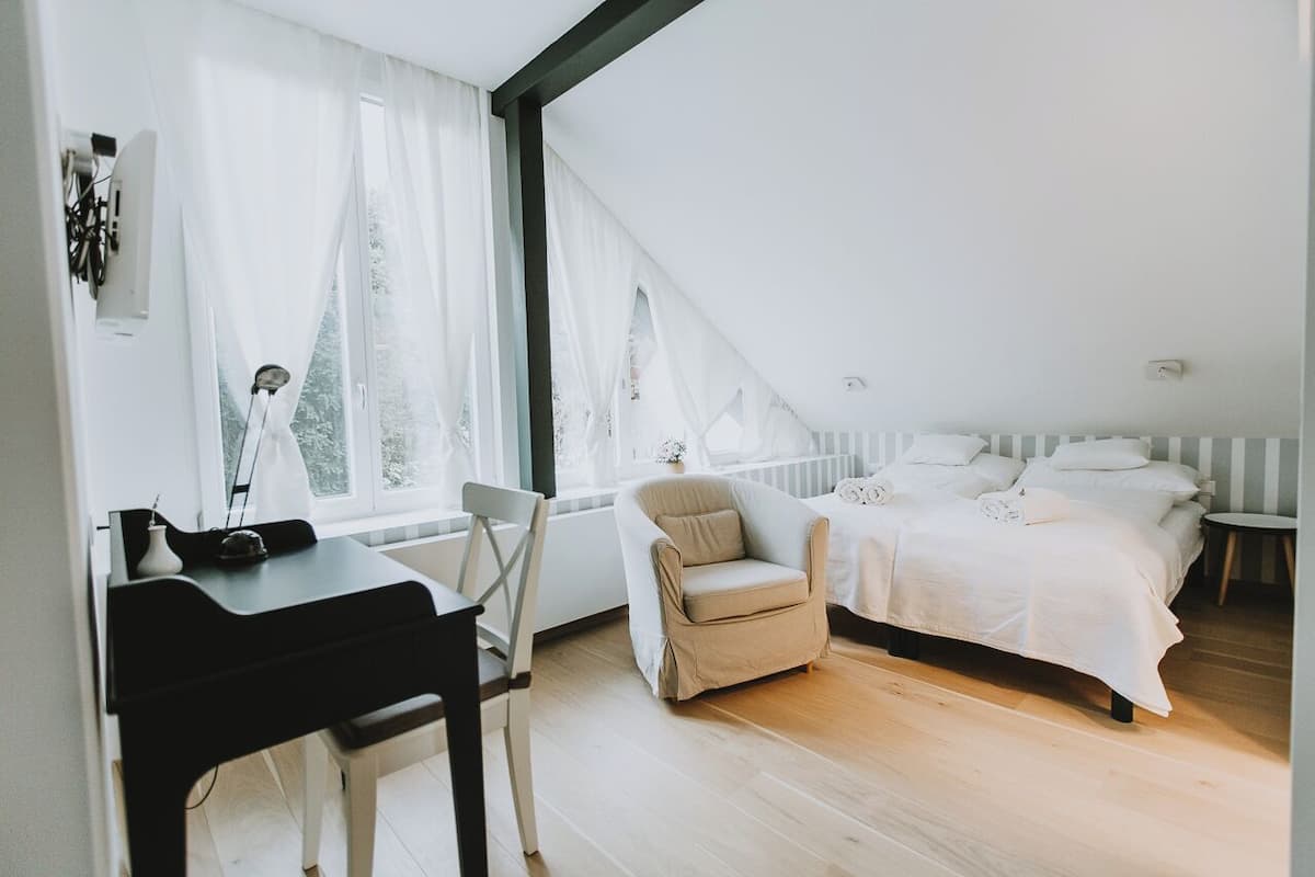 Un dormitorio con cama, escritorio, silla y ventana con cortinas.