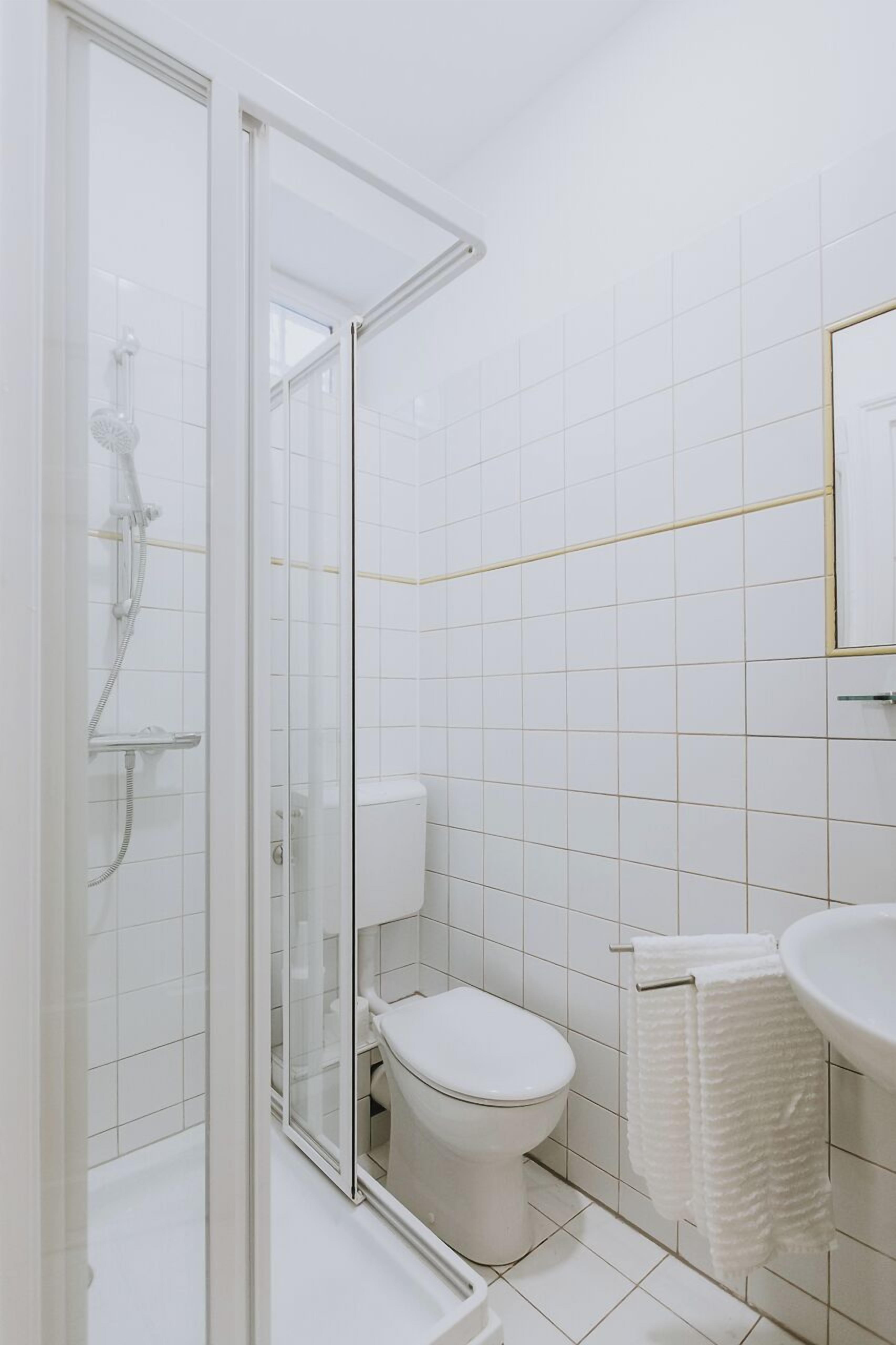 A bathroom with a glass shower enclosure, a toilet, and a sink with a towel hanging on the wall.