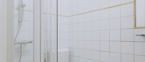 A bathroom with a glass shower enclosure, a toilet, and a sink with a towel hanging on the wall.