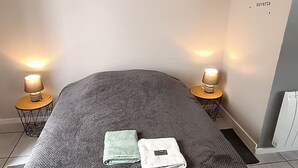 En snyggt bäddad säng med ett mörkgrått täcke och två hopvikta handdukar, två sänglampor och tre inramade silhuettbilder av djur på väggen.