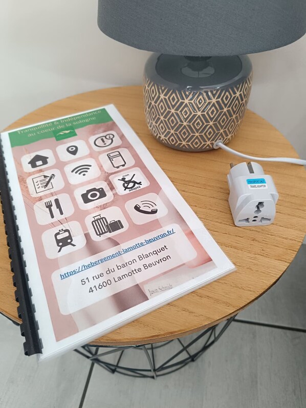 A brochure on a table with a lamp and a travel adapter. - "Le Loup" Studios Indépendant de Plein Pied Avec Terrasse , Proche du Centre (Lamotte-Beuvron)
