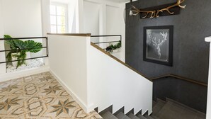 Un escalier moderne avec un sol à motifs géométriques, un mur foncé orné d’une paire de bois de cerf encadrés et un luminaire suspendu.