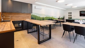 A modern kitchen with dark cabinets, a wooden countertop, and a mural of a forest on the wall. There are multiple tables and chairs arranged for dining. - Beautiful apartment in villa for 12 people with WIFI, hot tub, A/C, TV and patio (Balatonfüred)