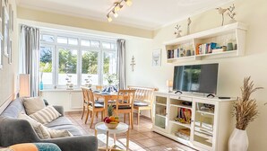 A living room with a sofa, dining table, chairs, a TV, and a bookshelf. - nur 100 m bis zum Strand, Zentrumsnahe Ferienwohnung - Villa Meernixe Fewo 10 (Ostseebad Binz)