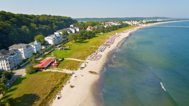 An aerial view of a coastal area with a beach, buildings, and a forested hill. - nur 100 m bis zum Strand, Zentrumsnahe Ferienwohnung - Villa Meernixe Fewo 10 (Ostseebad Binz)
