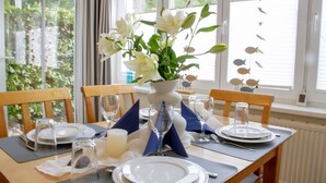 A dining table set for two with white plates, clear glasses, and a vase of white flowers. - nur 100 m bis zum Strand, Zentrumsnahe Ferienwohnung - Villa Meernixe Fewo 10 (Ostseebad Binz)