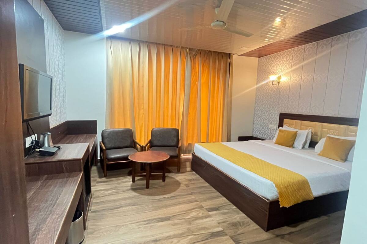 Hotelkamer met een bed, een bureau met een televisie, twee stoelen, een kleine tafel en een raam met gordijnen.