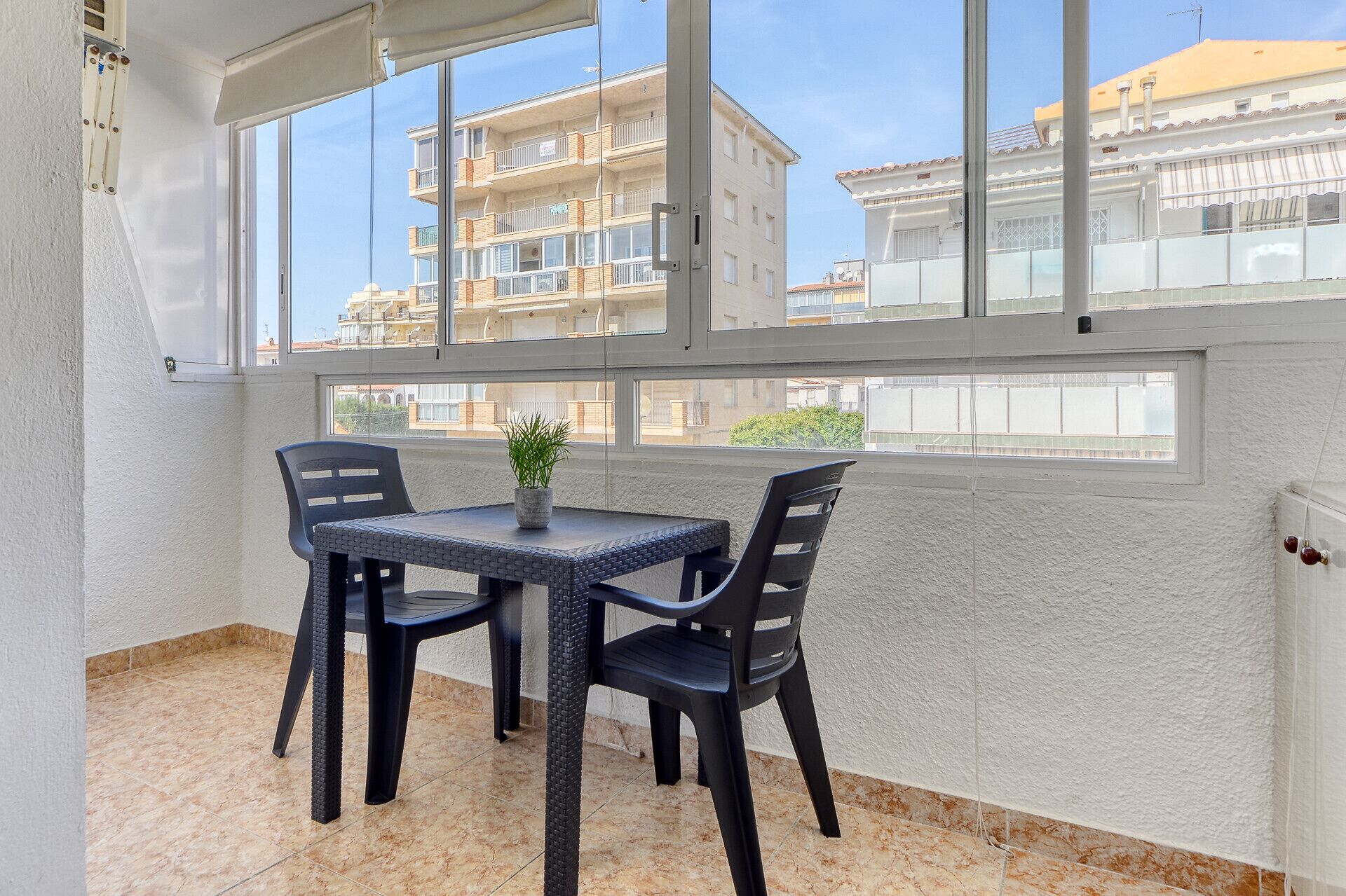 Ein Balkon mit Tisch und Stühlen, einem Blumentopf und Blick auf Wohnhäuser.