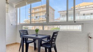 Un balcone con tavolo e sedie, una pianta in vaso e vista su edifici residenziali.