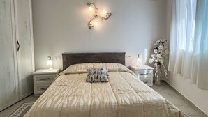 Un dormitorio con cama, mesitas de noche, una lámpara de pared y una ventana con cortinas.