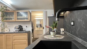 Una cocina moderna con armarios de madera, encimera negra y un fregadero. Hay una planta en maceta sobre la encimera y una pequeña mesa con un adorno.
