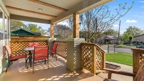 A covered outdoor patio with a table and chairs, a wooden fence, and a view of the neighborhood.