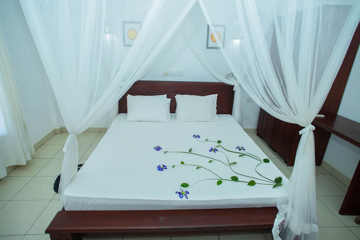 Una cama bien hecha con dosel, ropa de cama blanca y algunas flores azules sobre la cama.