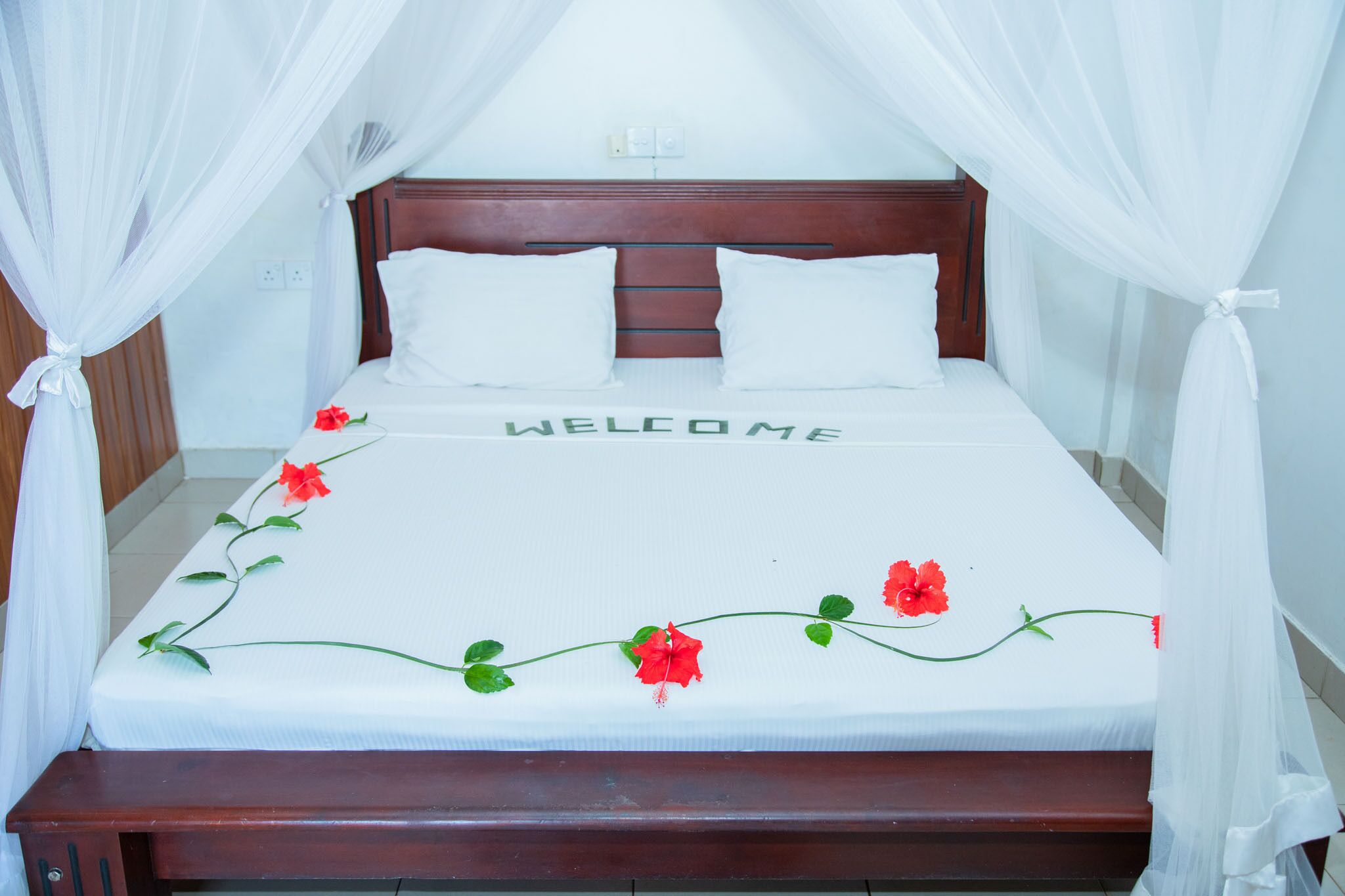 A bed with a white bedspread, two white pillows, and a "WELCOME" sign.