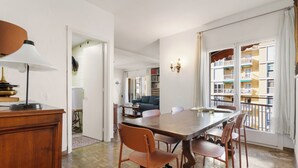 A dining area with a wooden table and chairs, a lamp, and a view of a balcony with buildings.