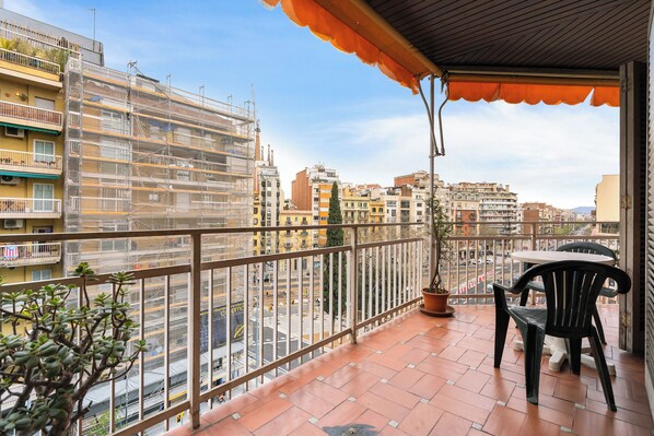 A balcony with a view of a cityscape, a potted plant, and a chair.