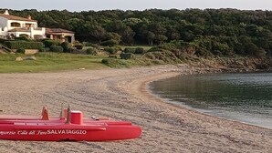 A beach with a lifeguard tower labeled "SALVATAGGIO" and a building in the background. - Porto Cervo Cala del Faro rent BILOCALE garden porch near the sea. (Porto Cervo)